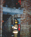 A firefighter prepares to assist a second firefighter just inside an upstairs apartment